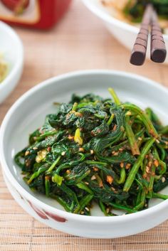 a white bowl filled with green vegetables next to chopsticks and other food items