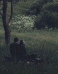 two people sitting in the grass under a tree