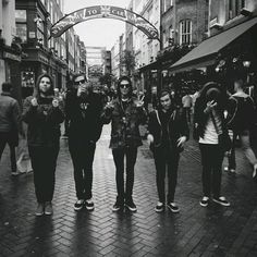 black and white photograph of four people standing in the middle of a street under an arch