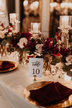 the table is set with gold plates and red napkins, candles and floral centerpieces