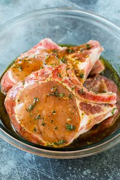 two raw meats in a glass bowl with sauce and parsley on the side