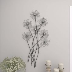 a metal wall sculpture with flowers on it next to candles and a vase filled with baby's breath