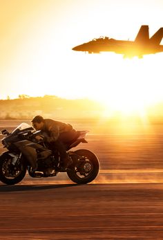 a person riding a motorcycle in front of an air force jet flying over the ground