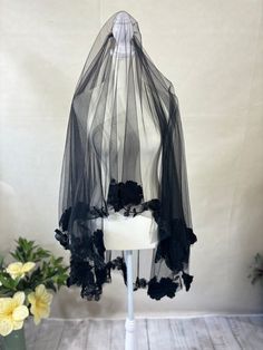 a white mannequin wearing a black veil with flowers on it's head