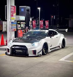 a white nissan sports car parked in front of a gas station at night with its lights on