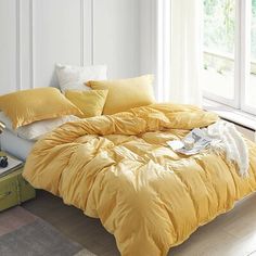 a bed with yellow comforters and pillows in a room next to a window,