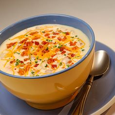 a bowl of soup with bacon and cheese in it on a blue plate next to a silver spoon