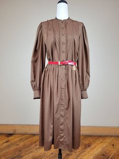 "Brand: Adele Simpson  Size: 26\" waist; see measurements  Color: brown/red Fabric Content: Polyester    Features:  Beautifully constructed Adele Simpson dress with numerous designer details. Shirtwaist dress with six rows of miniature pleats at bodice front, neckline and the cuffs. Front is closed with covered buttons. Long sleeves are elegantly gathered at the shoulder and wrist. Bodice back has shoulder darts for tailored fit. Gathered skirt is stitched to the gathered bodice at the waist. Matching patent leather belt.   Measurements: Neck: 14in  Bust/Chest:36in  Waist: 26in  Belt: 27in-32  Hip: 38in  Shoulder to Shoulder: 14in  Sleeve  Length: 24in  Center Back Length: 44in    Condition: Very Good Vintage Condition - skirt hem has been professionally repaired.   Care: Dry clean only  V Retro Vintage Dress For Fall, 1970s Vintage Dress For Fall, Brown Long Sleeve Vintage Dress For Spring, 1970s Fitted Brown Dress, Fitted Brown 1970s Dress, Fitted Brown 1970s Style Dresses, 1970s Style Fall Workwear Dresses, Classic Long Sleeve Brown Dress, Vintage Brown Midi Length Dress