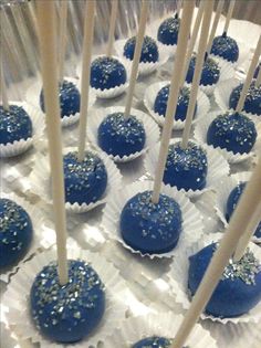 blue cake pops with white sprinkles and sticks on a tray covered in plastic wrappers