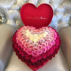 a heart shaped box filled with roses on top of a white couch next to a pillow