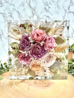 a vase filled with lots of flowers on top of a wooden table covered in greenery