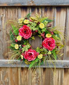 a wreath with red and yellow flowers hanging on a wooden fence next to some plants