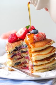 a stack of pancakes with berries and syrup being drizzled on top