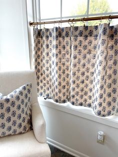 a white chair sitting in front of a window next to a blue and white curtain