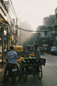 two men pushing a cart full of fruit down the street