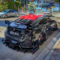 a black car parked on the side of a road next to a street with cars behind it