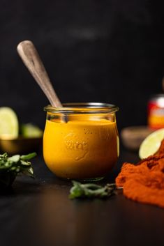 a glass jar filled with yellow liquid next to some spices and limes on a table