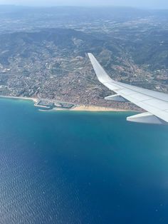 an airplane wing flying over the ocean and land