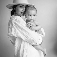 a woman holding a baby in her arms and wearing a hat on top of her head