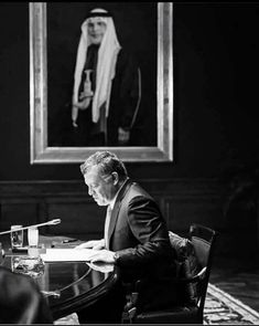 a man sitting at a table in front of a painting with a portrait on it