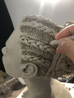 a person is working on a clay head with crochet work in the shape of a woman's head