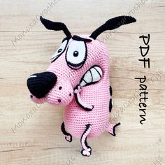 a crocheted pink dog with black nose and tail holding another dog's head