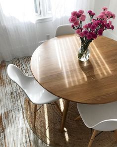 a wooden table with white chairs and pink flowers in a vase on top of it