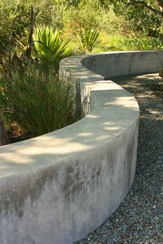 a concrete bench sitting on top of a gravel road next to trees and bushes in the background