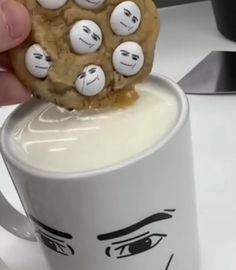 a person holding a cookie in their hand over a coffee mug with faces on it