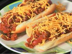 two chili dogs on buns with cheese and ketchup sitting on a plate