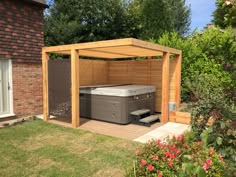 a wooden gazebo with a hot tub in the middle and flowers around it outside