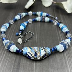 This necklace started with the incredible 19x35mm artisan lampwork focal. This piece provided many gorgeous shades of blue to pull from. I did this with 4.5mm starcut kyanite, 6mm lapis rondelles, 7mm faceted larimar rondelles, rainbow moonstone rondelles ranging from 7-9mm, 10.5mm kyanite slices, 12mm lodalite discs, 7.7x7mm faceted czech glass, sterling silver spacers, and 9.5mm etched artisan glass rondelles. Hanging from the end of the extender chain is an incredible little drusy quartz for that extra special touch. The rainbow moonstone are flashy but apparently very camera shy!This necklace is sterling silver with a lobster clasp and extender chain that allows the necklace to adjust from 18 - 21”. Blue Gemstone Necklace, Camera Shy, Blue Gemstones, Rainbow Moonstone, Gemstone Necklace, Czech Glass, Shades Of Blue, Moonstone, Shades