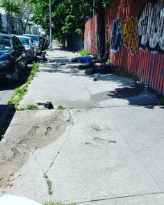 the sidewalk has been vandalized with grafitti and is lined with parked cars