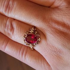 a woman's hand holding a ring with a large red stone in the middle