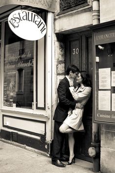 a man and woman kissing in front of an italian restaurant on the corner of a street