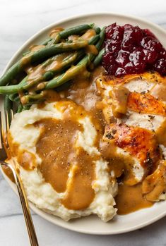 a plate with mashed potatoes, green beans and gravy next to cranberry sauce