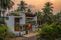 an apartment building with palm trees in the foreground and a sunset sky behind it