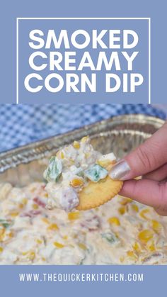 a hand holding a cracker over a casserole dish filled with corn dip