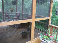 a screened porch with potted plants and chairs on the back deck, looking out onto the woods