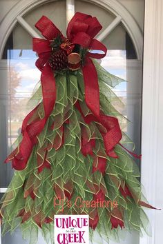 a red and green christmas tree hanging on the front door with a sign underneath it