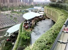 people are sitting at tables in the middle of an area with green plants on it