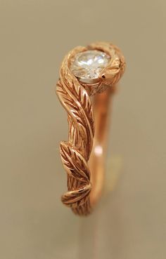 a gold ring with leaves on it and a diamond in the center, sitting on a table