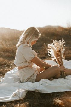 a woman sitting on top of a blanket holding a vase with dried flowers in it