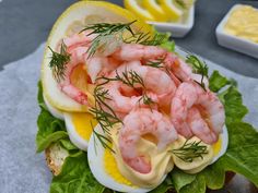 an open faced sandwich with shrimp and lettuce on it next to lemon wedges