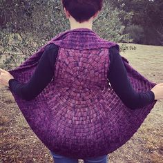 a woman wearing a purple shawl standing in front of an apple tree with her back to the camera