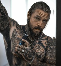 a man with tattoos on his chest holding a cell phone and pointing at the camera