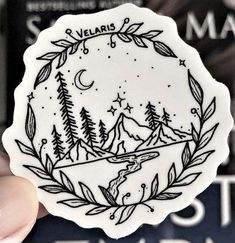 a person holding up a sticker with trees and mountains on it