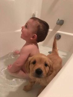 a baby sitting in a bathtub next to a brown dog with it's head on the tub