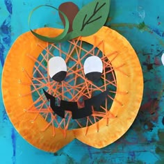 a paper plate pumpkin with yarn wrapped around it's face and eyes, sitting on a blue surface