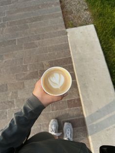 a person holding a cup of coffee in their hand on the sidewalk next to a brick walkway